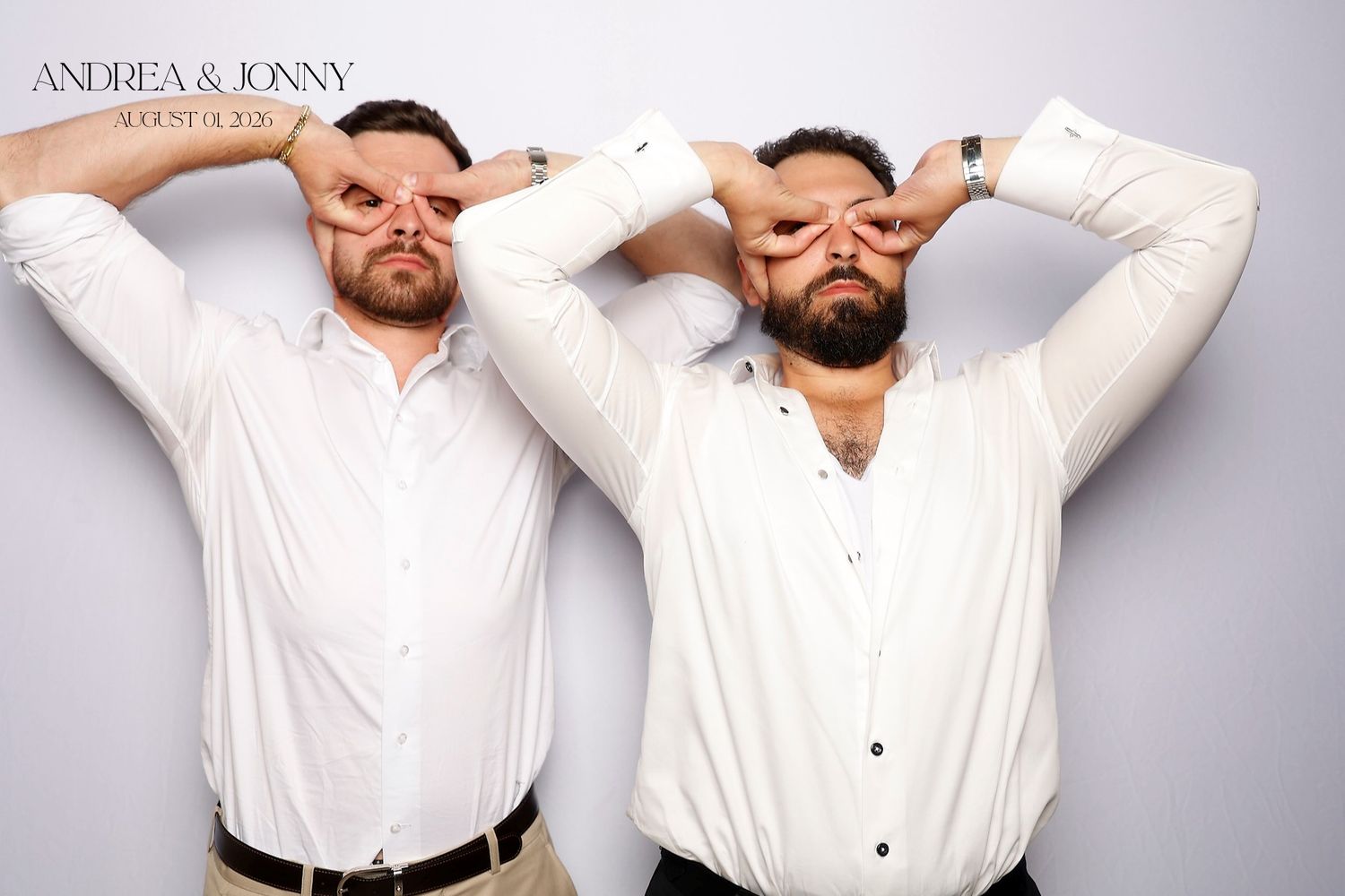 Two men in white shirts pose playfully at Andrea and Jonny wedding photo booth, making glasses with their hands over their eyes.