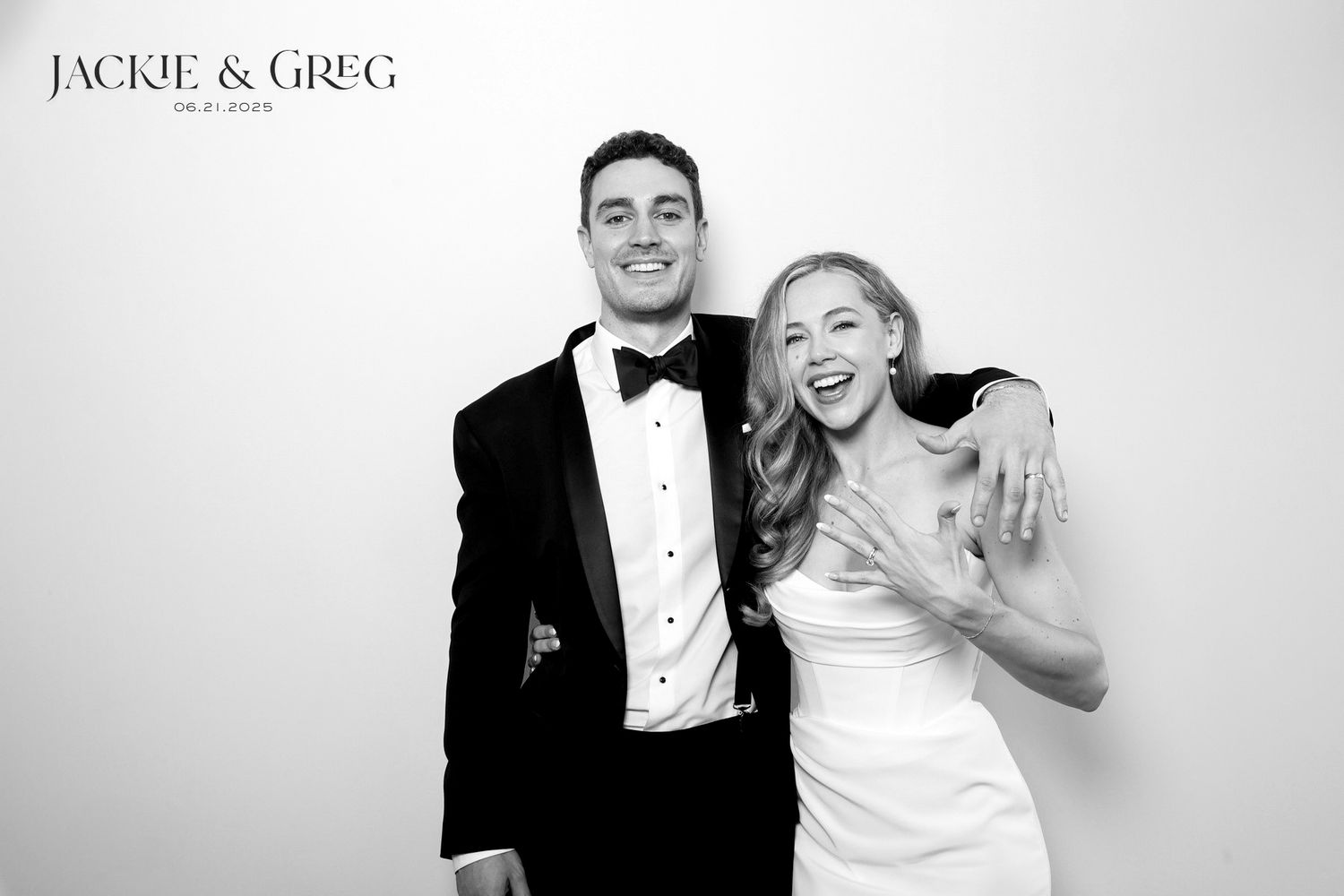 Black and white photo of a happy couple in formal wedding attire laughing together against a plain background.