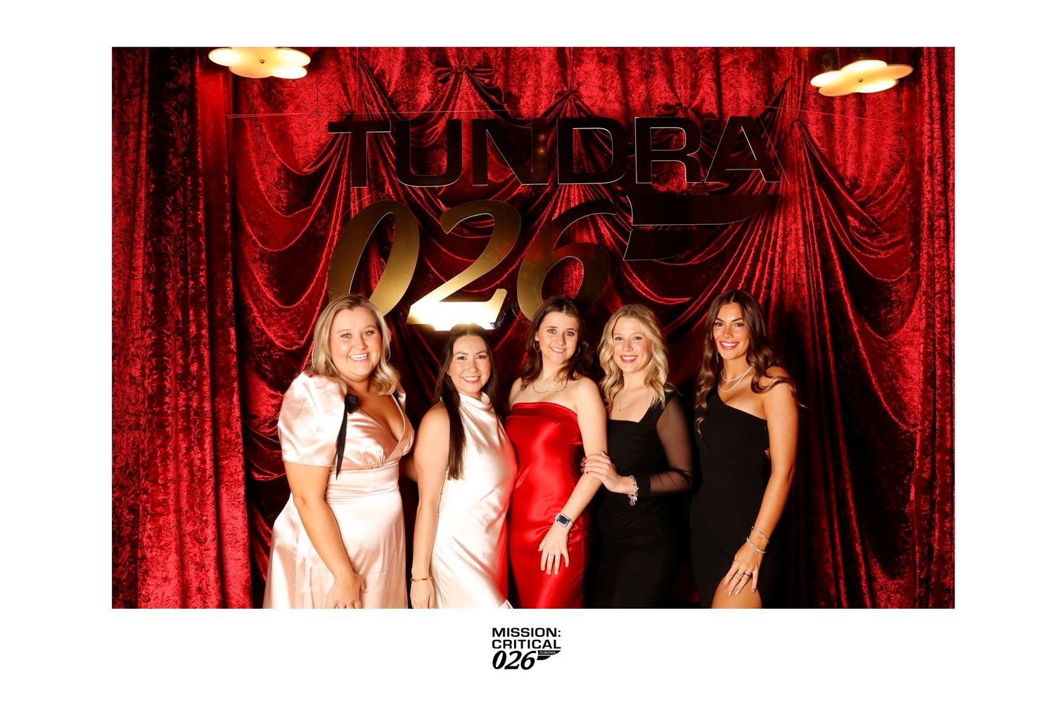 Group poses together in front of red curtain backdrop at formal event.