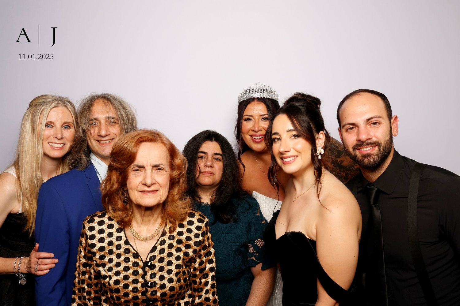 A group of seven people pose together at a photo booth against a gray backdrop.