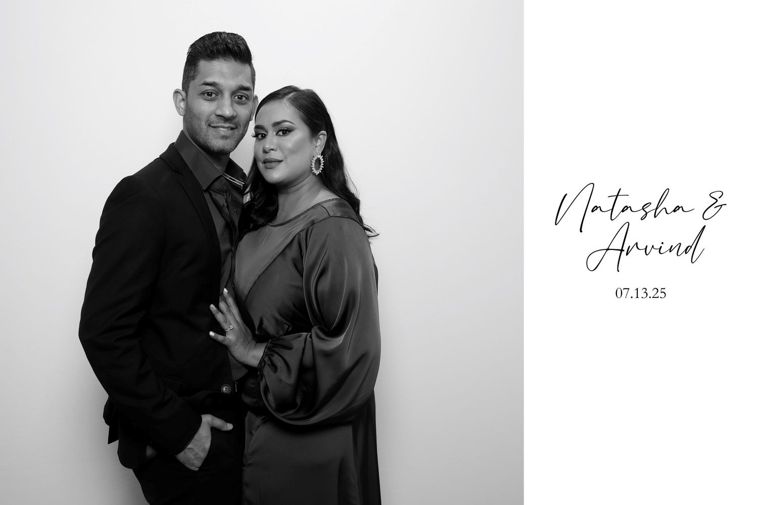 A fashionable couple poses together in black and white studio portrait with elegant attire and signature text.