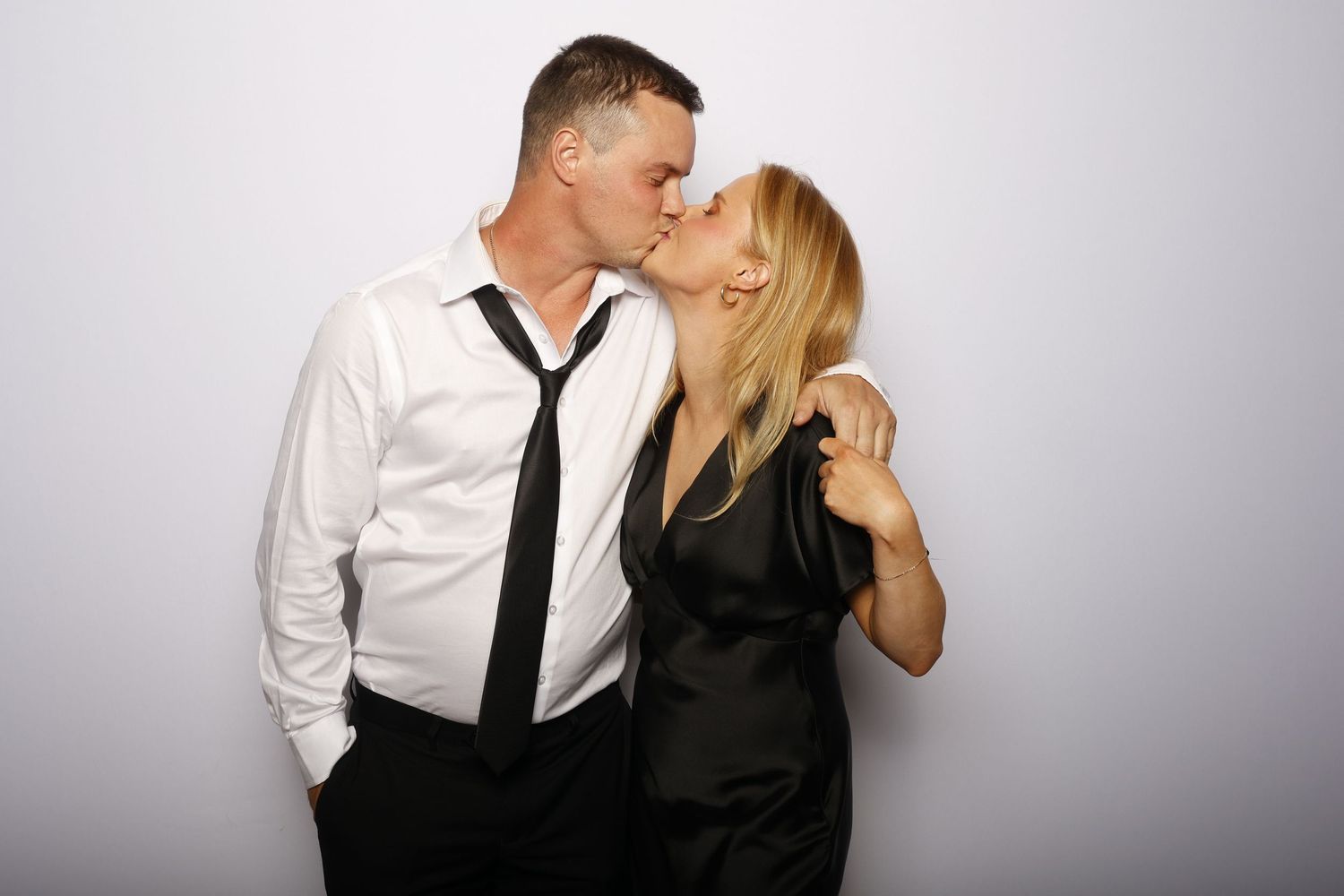 A couple in formal black and white attire embracing in a romantic pose against a light background.