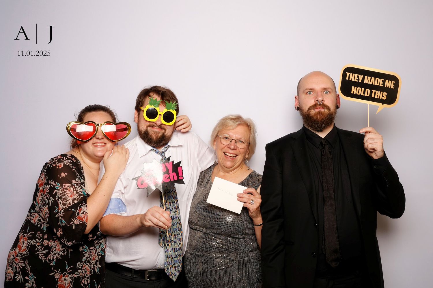 A group of four people pose together at a photo booth wearing fun sunglasses and holding signs.