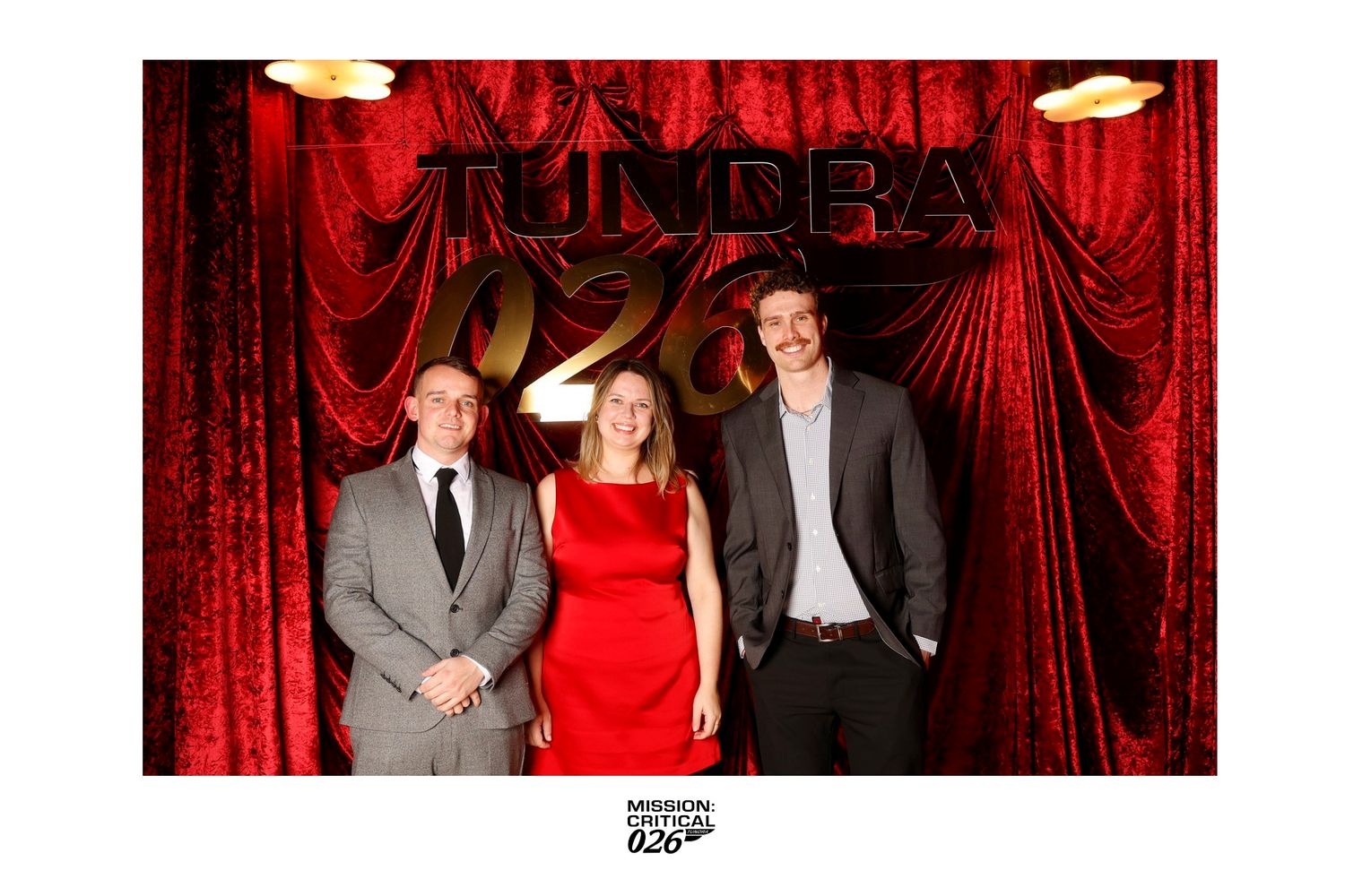 People pose for photos against a red curtain backdrop at a formal event.