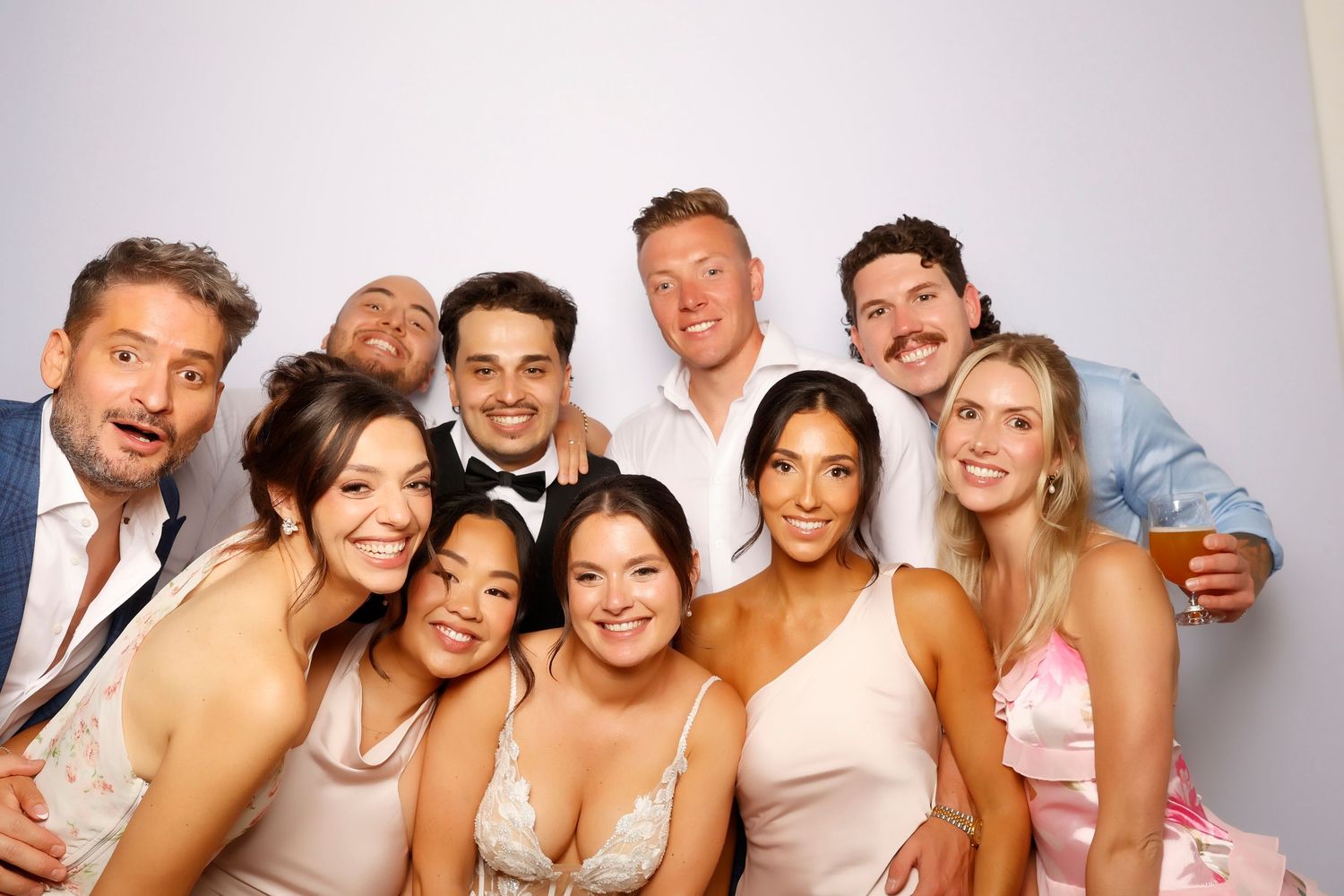 Group of friends posing together at a wedding celebration, smiling in formal attire against a white background.