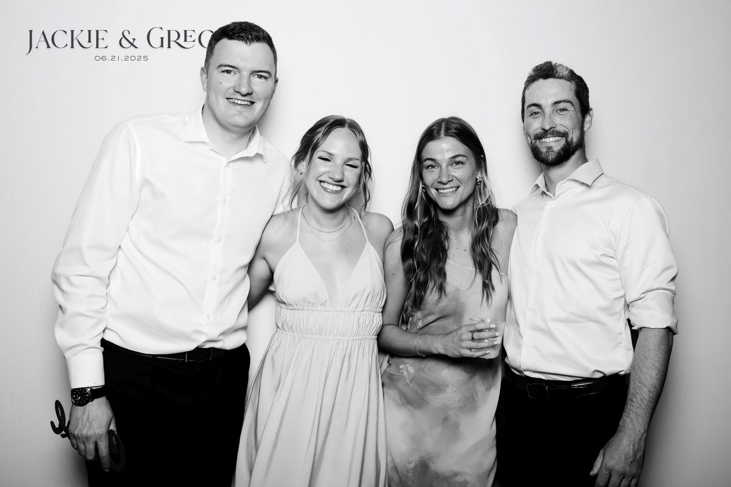 Black and white photo of two couples posing together at a wedding event, dressed in formal white attire.