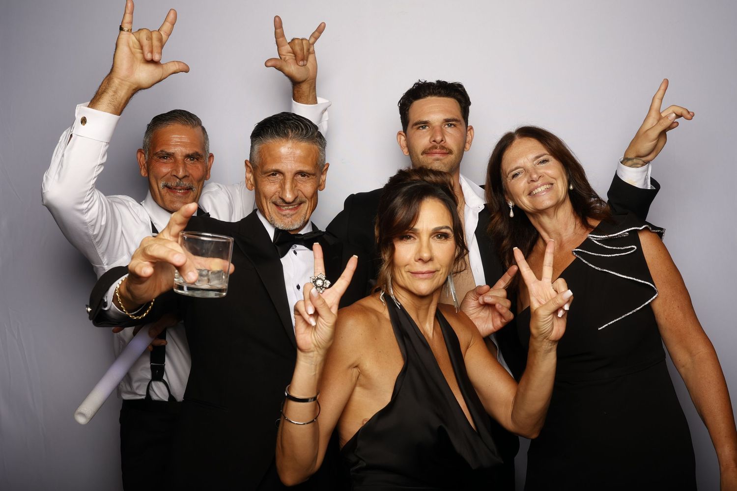 Group of people at a party making rock and roll hand gestures while posing for photos in a photo booth.