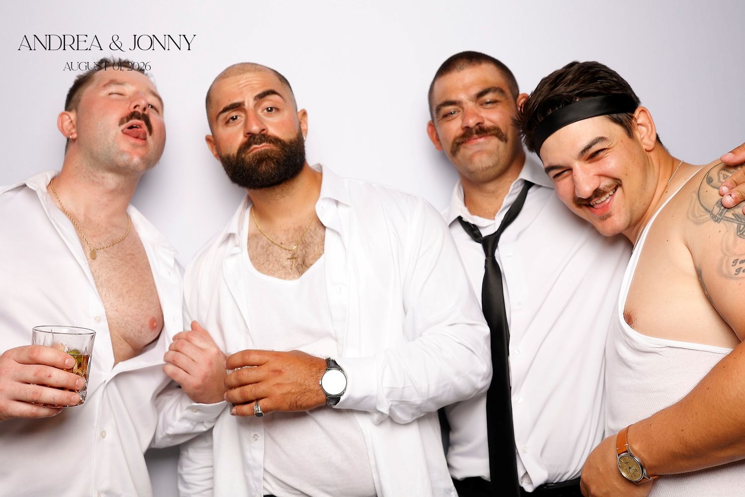 Four men in white shirts pose playfully at Andrea and Jonny wedding photo booth, one wearing a black tie.