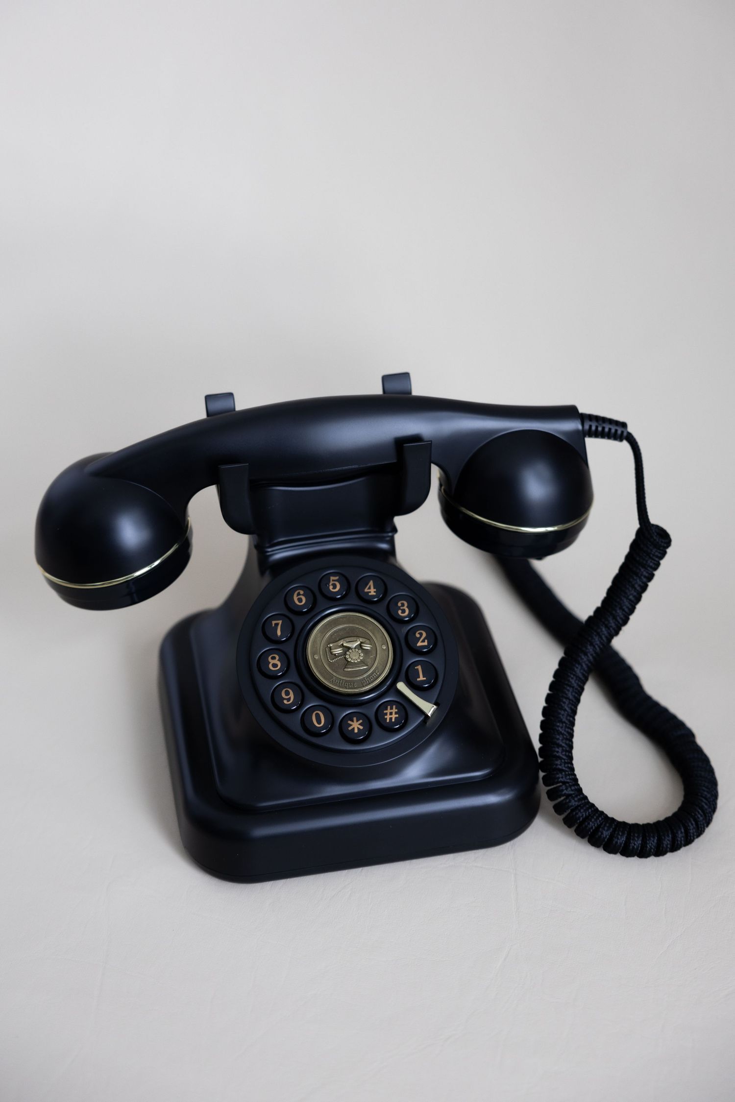 Vintage black rotary telephone with coiled cord on light gray background.