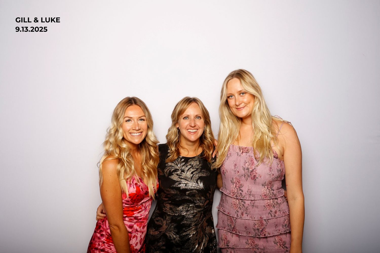 Three women in elegant evening attire pose together for a photo against a light gray background.