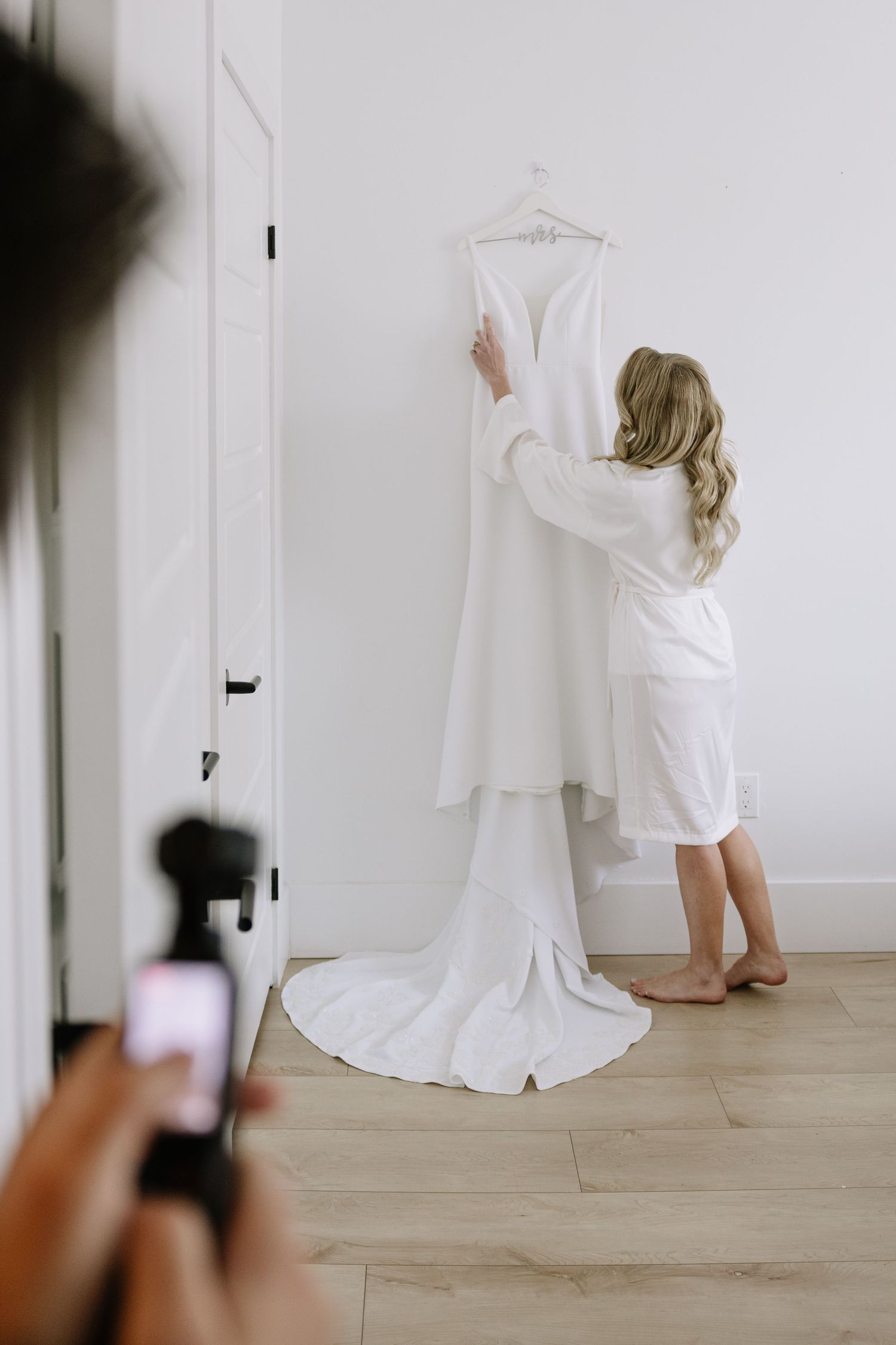 Four sequential photos showing someone in white clothing reaching up to adjust a hanging garment display on a white wall.