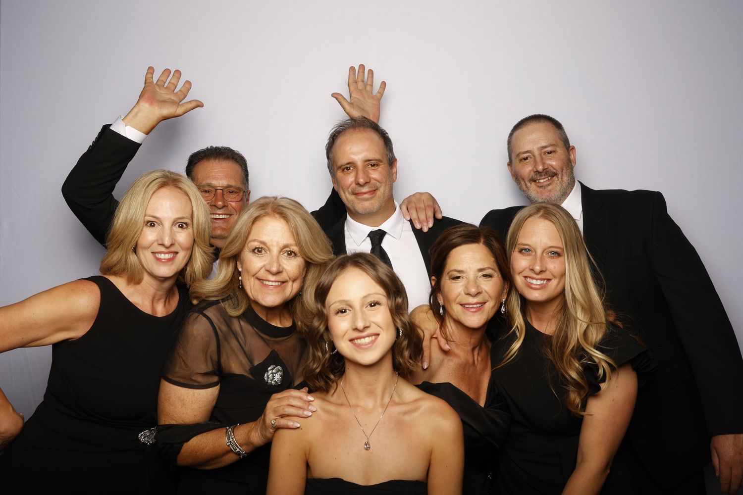 A group of friends pose together at a photo booth wearing formal black attire and smiling at the camera.