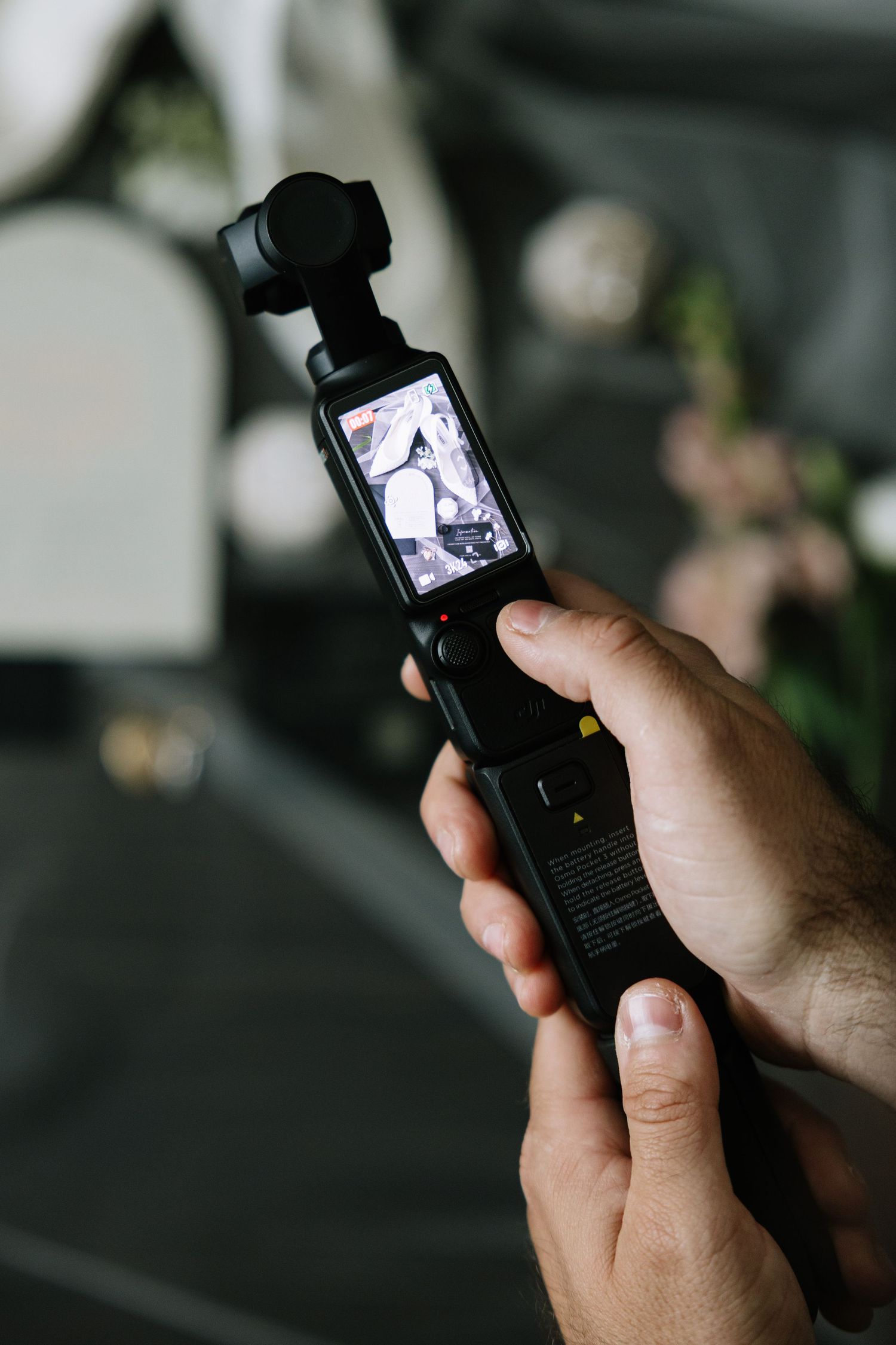 Hand holding DJI Osmo Pocket camera with LCD screen displaying video preview in monochrome.