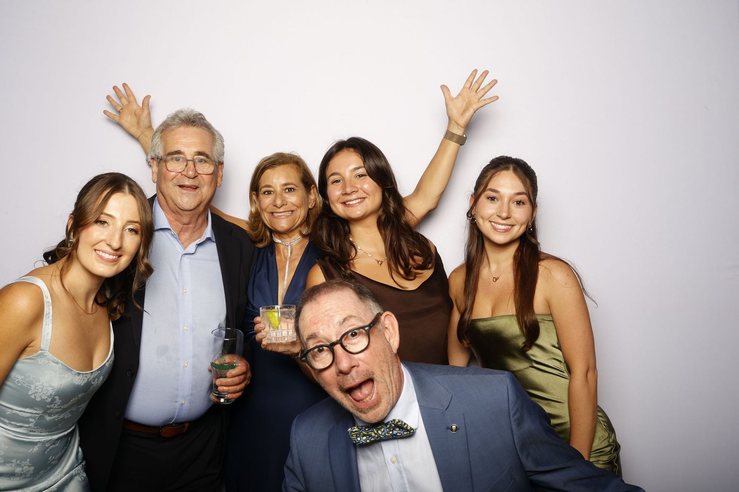 A group of people pose together in a photo booth setting with festive expressions and celebratory gestures.