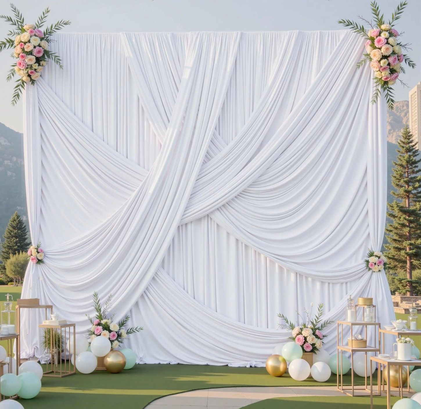 Elegant outdoor wedding ceremony setup with white draped fabric backdrop and floral arrangements against a mountain view.