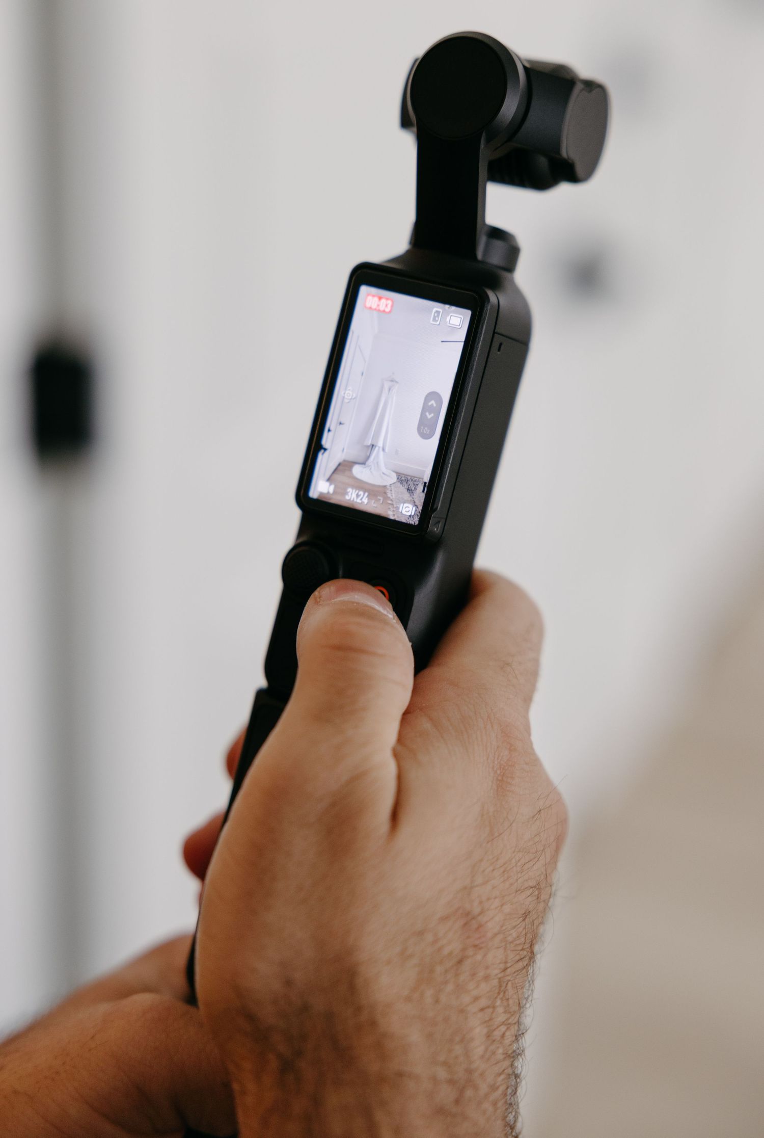 Hand holding a DJI Osmo Pocket camera showing small LCD screen display in close-up view.