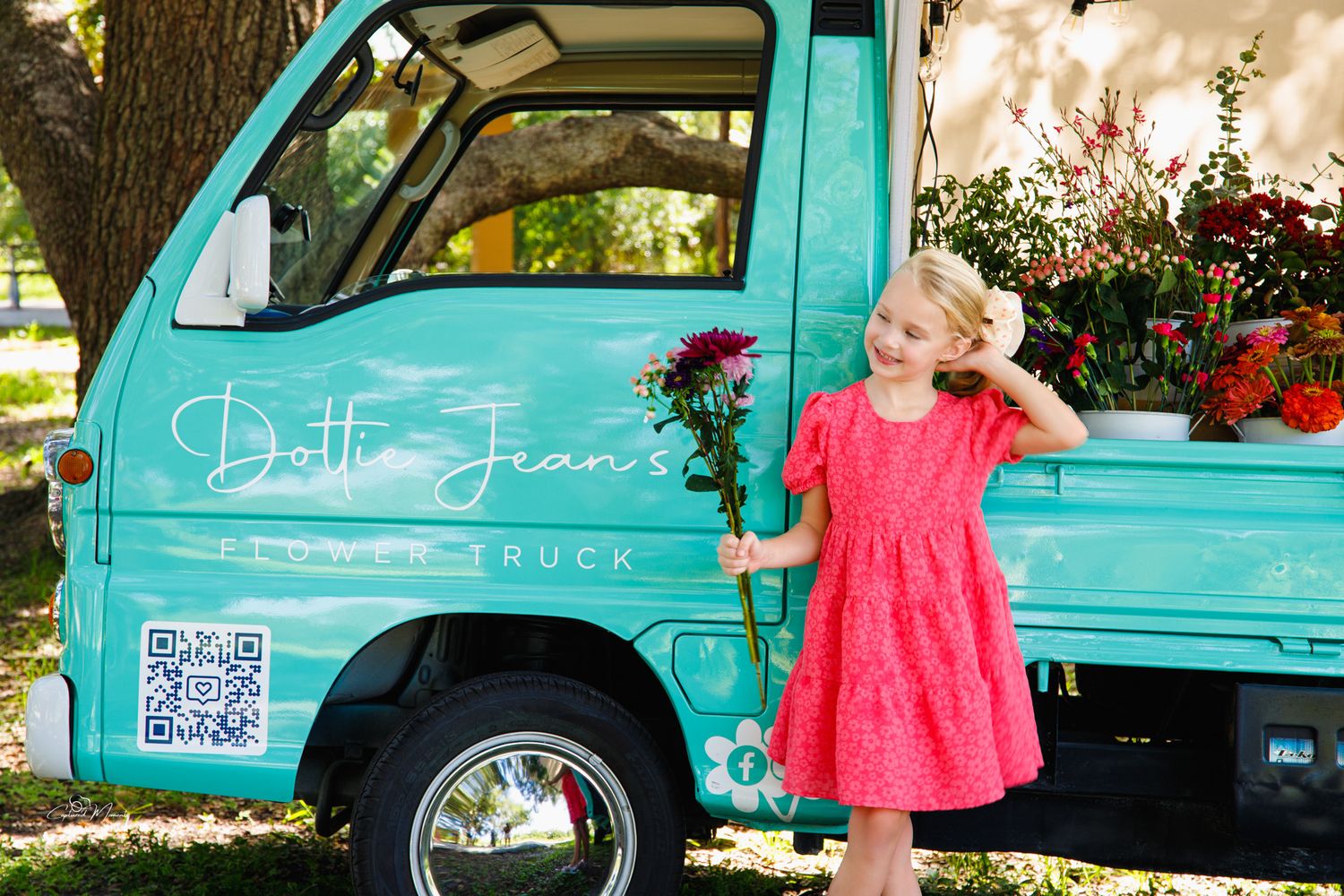 Young girl smiling beside a vintage flower truck during a spring portrait session photographed by Captured Moments Photography.