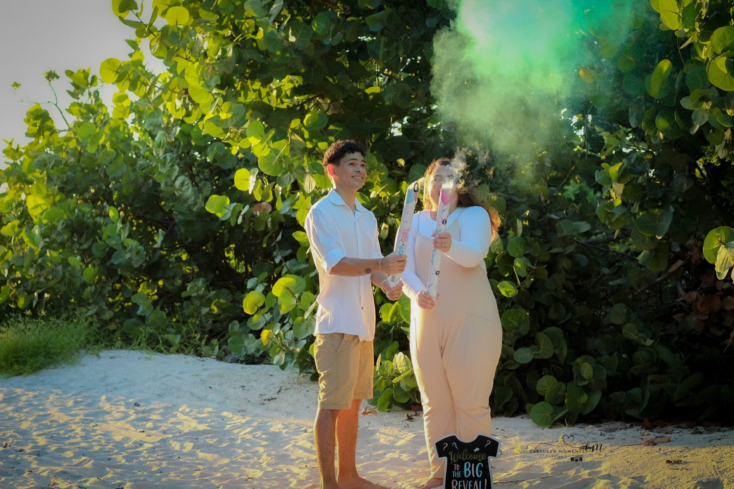 Couple celebrating their gender reveal at the beach with colorful smoke and joyful smiles during a maternity reveal session captured by Capt