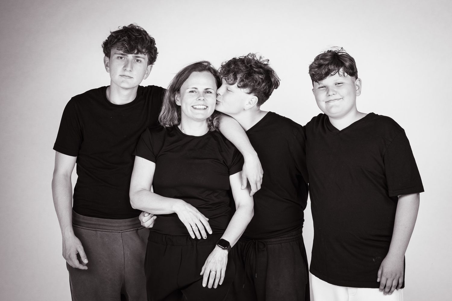 Black and white family portrait of a woman and three teenage boys wearing matching black shirts, smiling together.