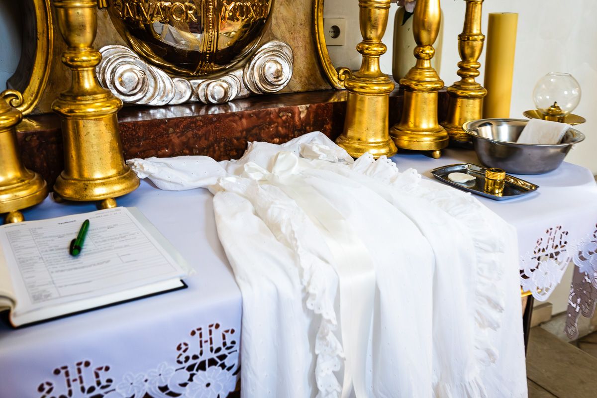 White baptismal gown on church altar with golden candlesticks, registry book, and ceremonial bowl for christening.