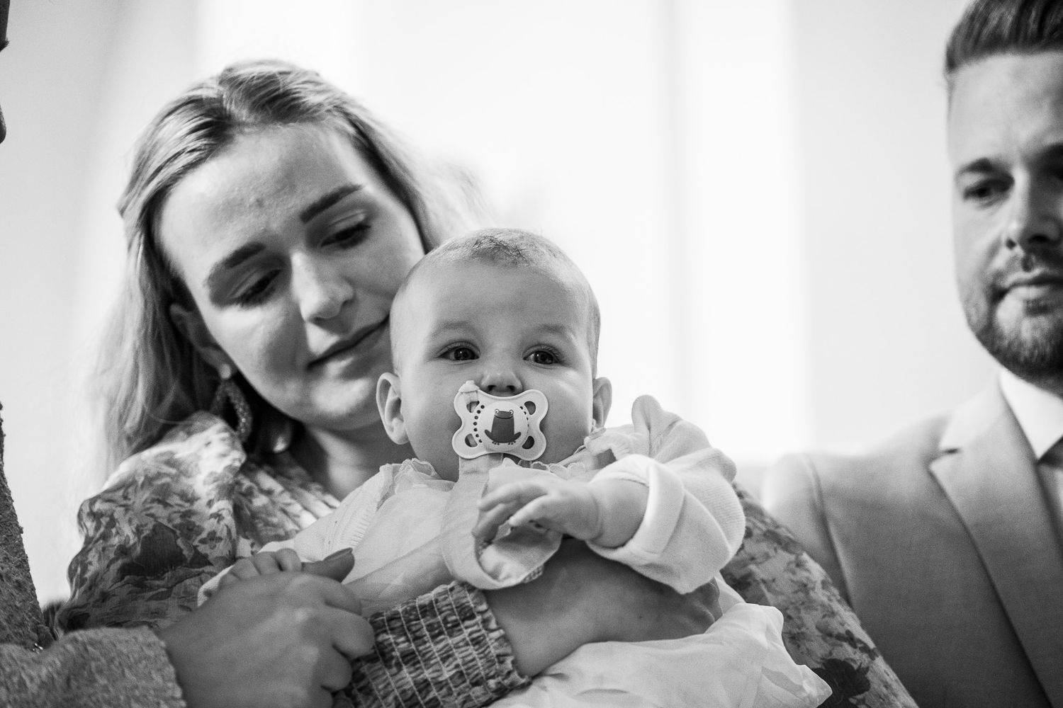 Black and white photo of a mother holding her baby with a pacifier at a christening ceremony.