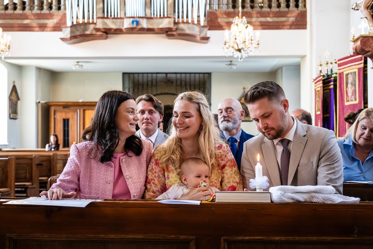 Family gathered in church for a baptism ceremony, with parents holding baby near the altar with a lit candle.