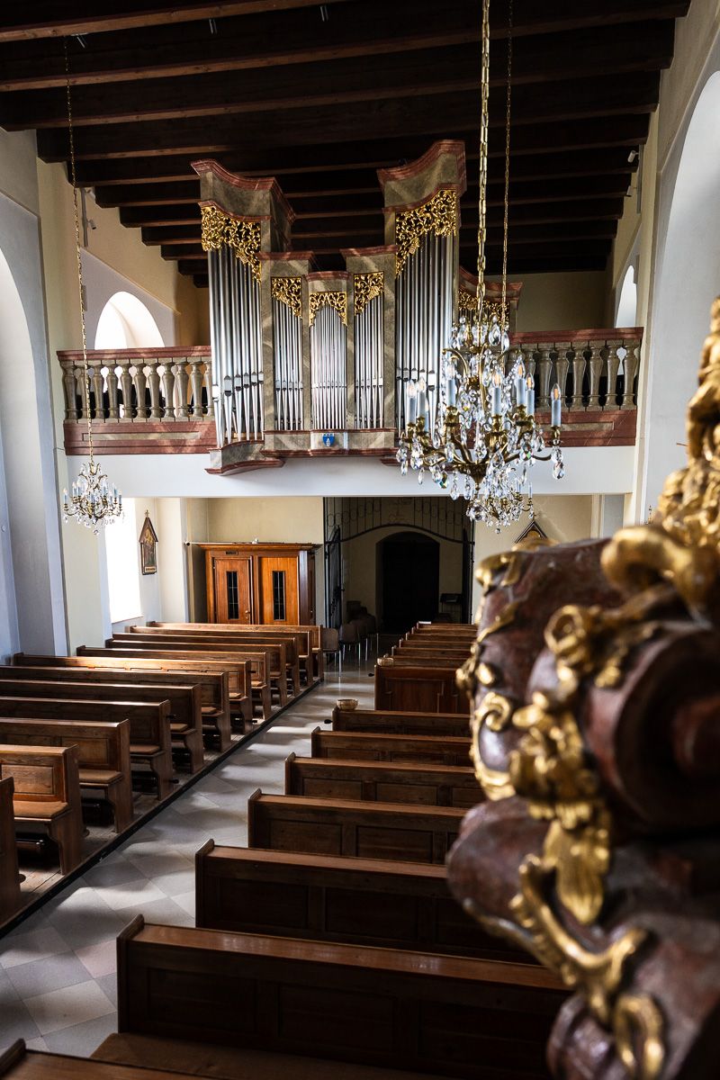 Elegant historic church interior featuring wooden pews, crystal chandeliers, and a ornate pipe organ on the upper balcony.
