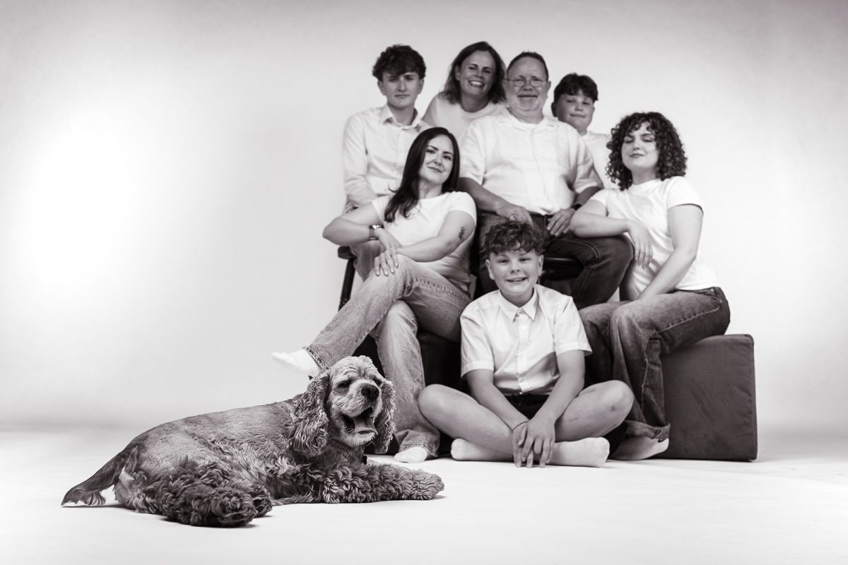 Black and white family portrait with parents, children, and a Cocker Spaniel dog posing together in a studio.