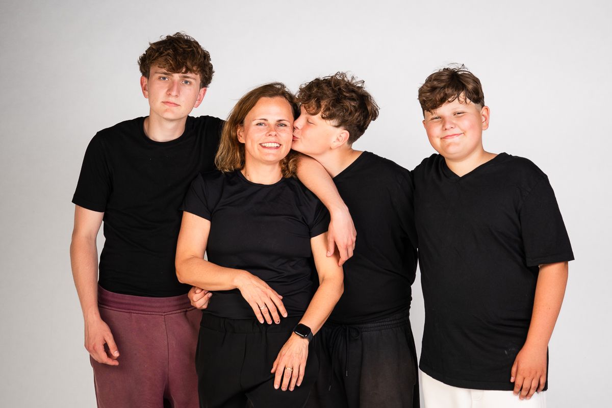 A woman and three boys in black shirts pose together smiling in a studio portrait photo.