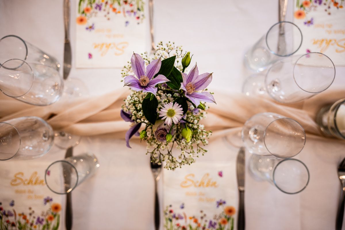 Elegant wedding table setting with purple lily bouquet, daisies, wine glasses, and floral menu cards.