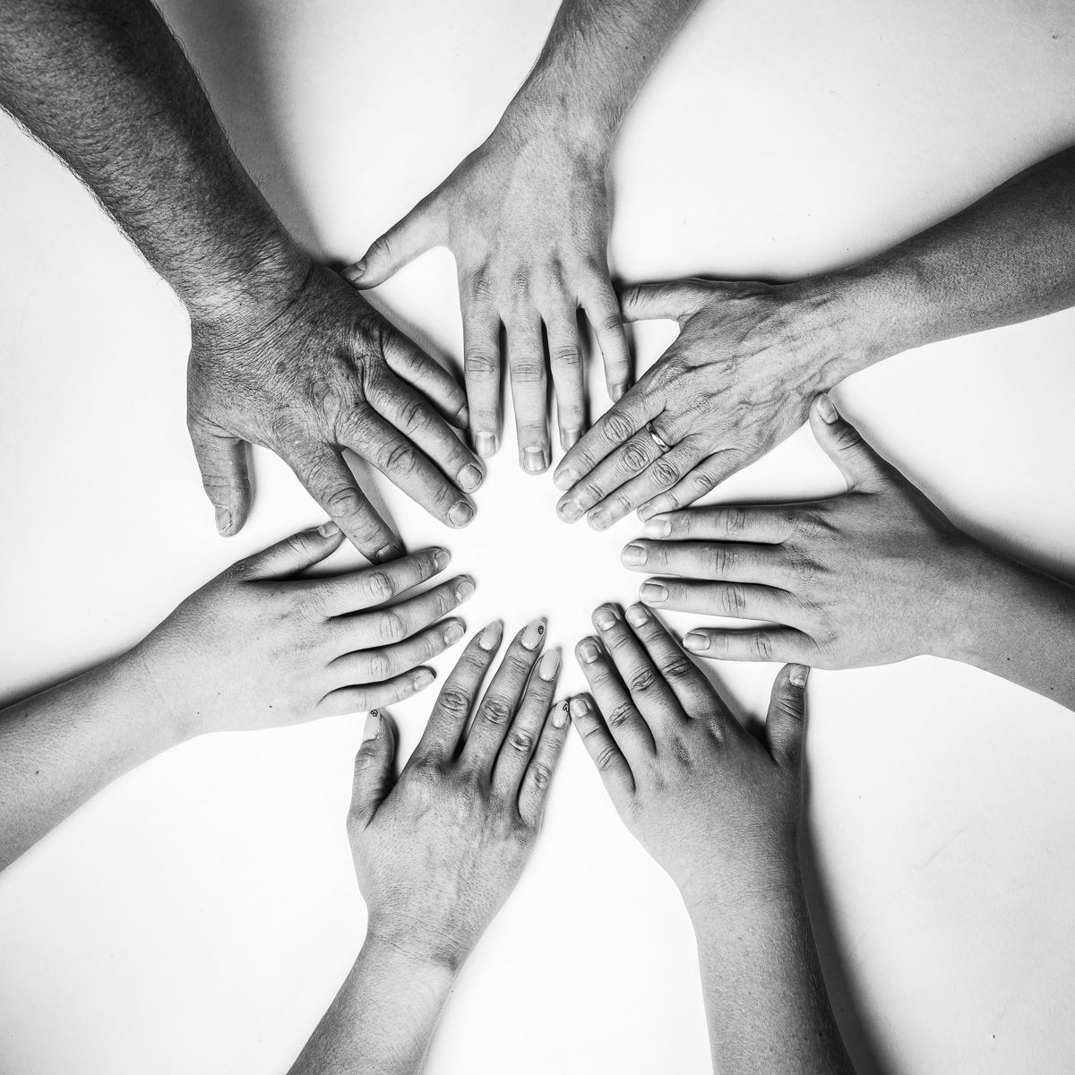 Black and white photo of diverse hands joined together in a circle, symbolizing unity, teamwork, and collaboration.