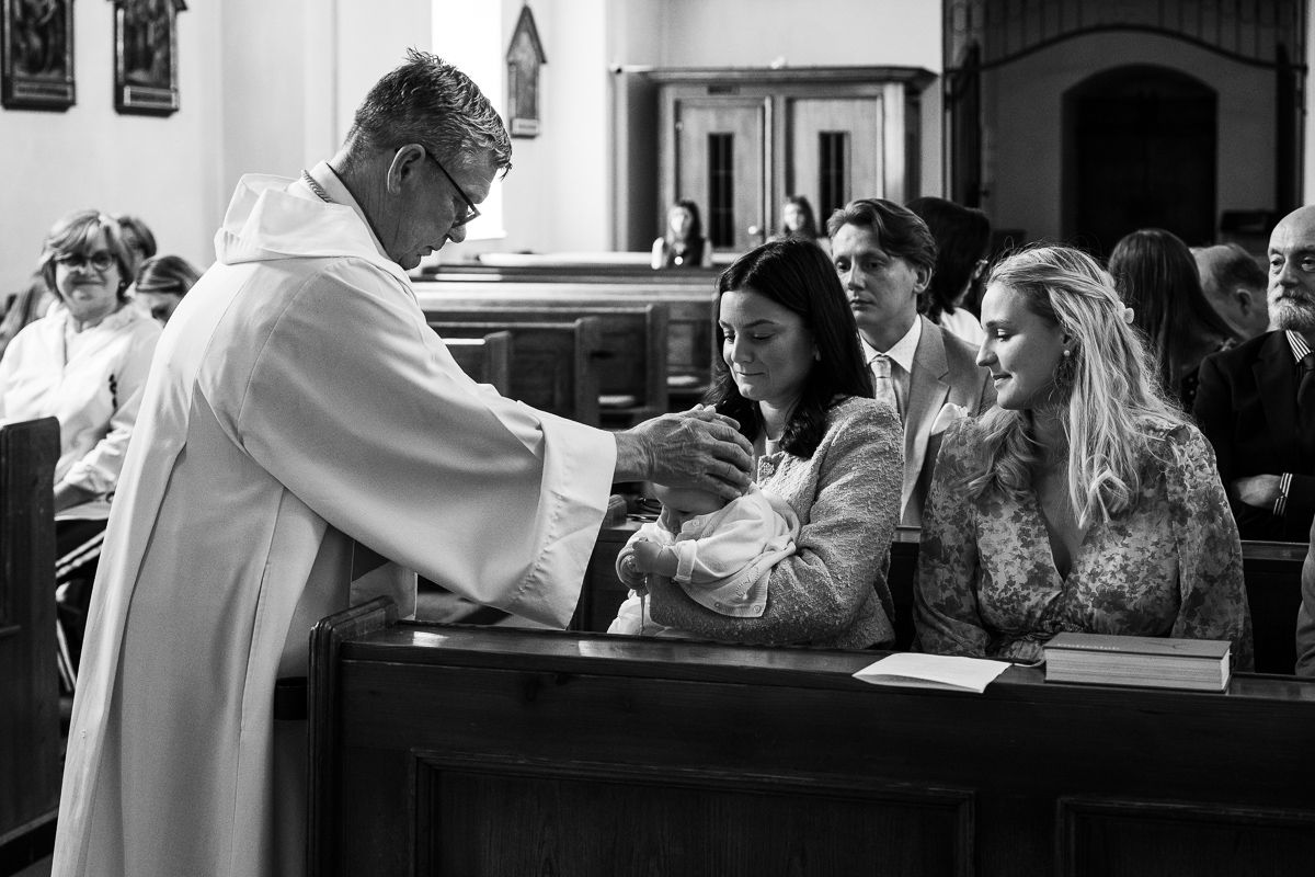 Priest performing a religious ceremony with two women in a church pew, black and white photography.