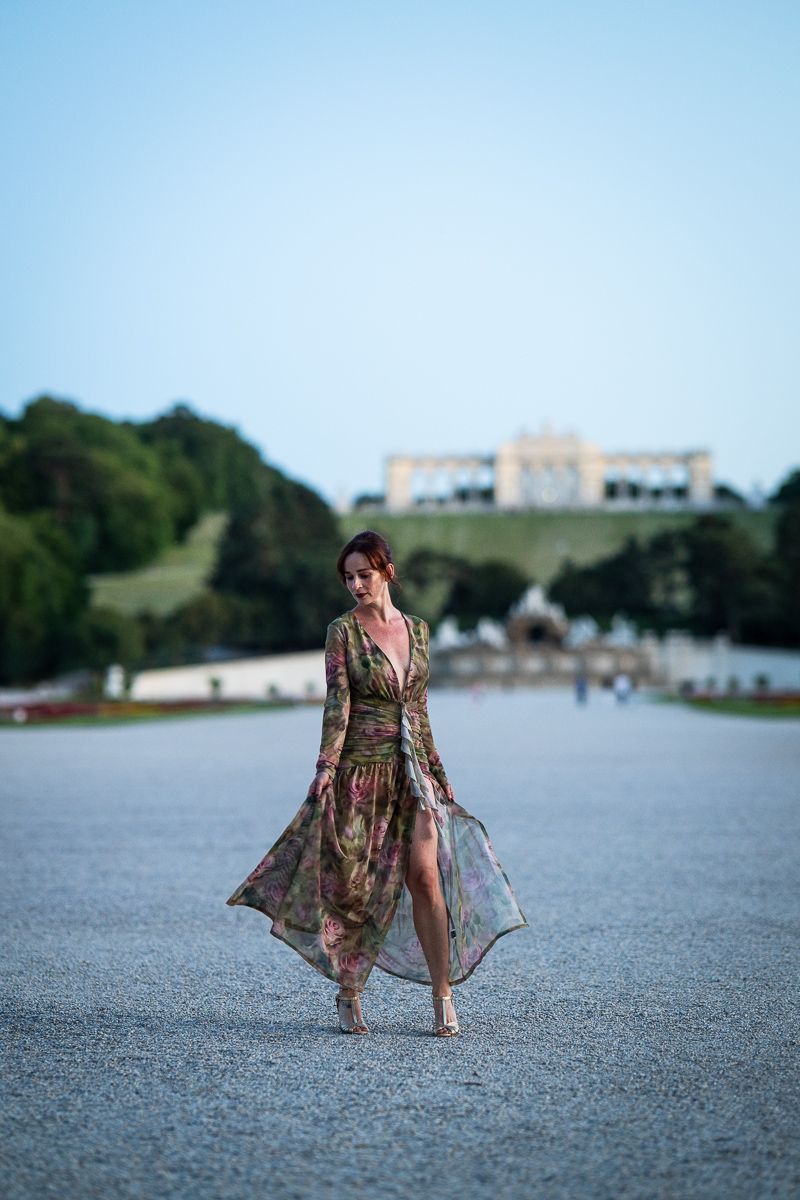 Woman in floral gown walks gracefully at Schönbrunn Palace gardens, Vienna.