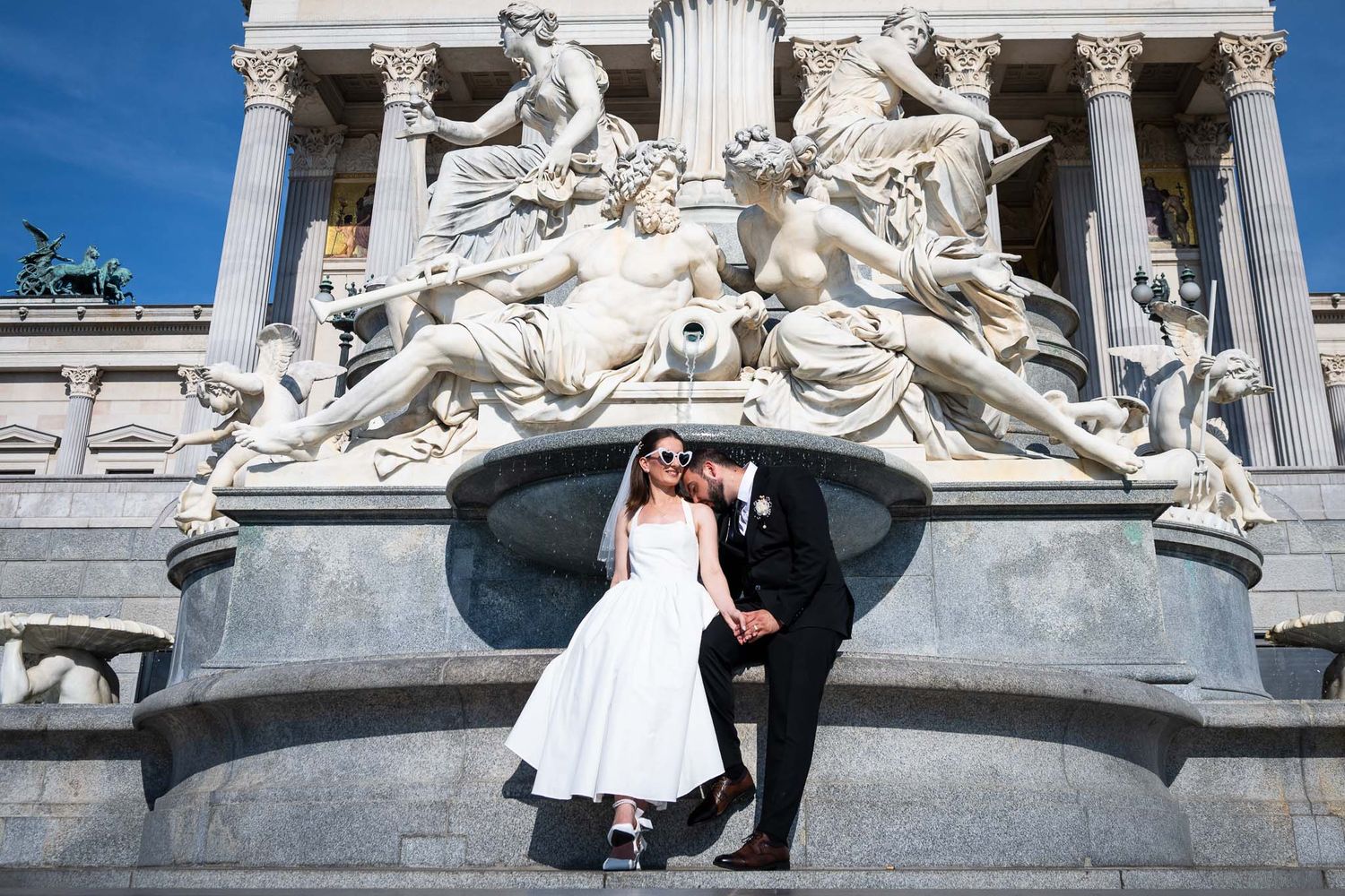 Bride and groom pose in front of ornate classical sculpture at elegant European monument on their wedding day.