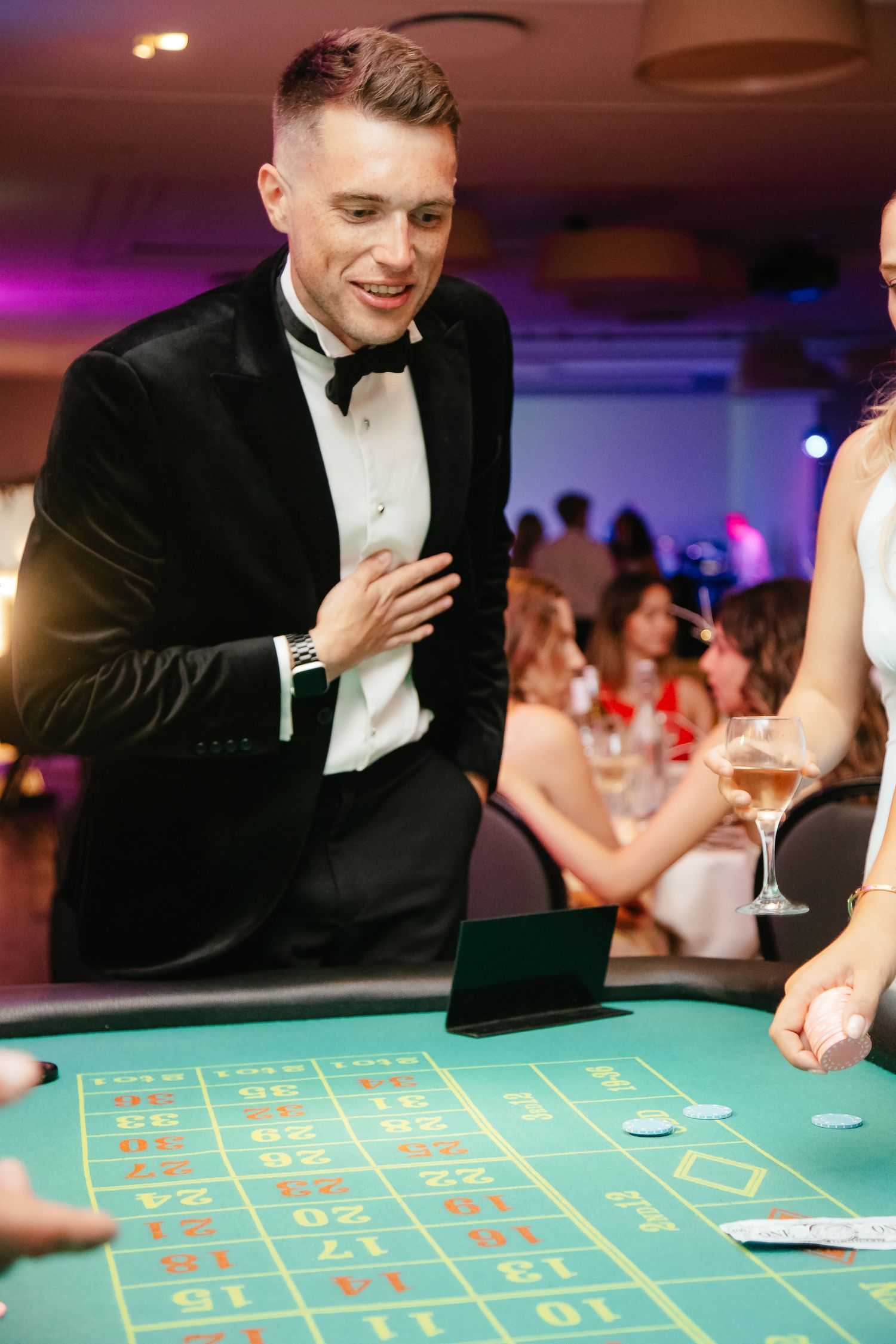 Formal event at a casino featuring tuxedo-clad players at a roulette table.