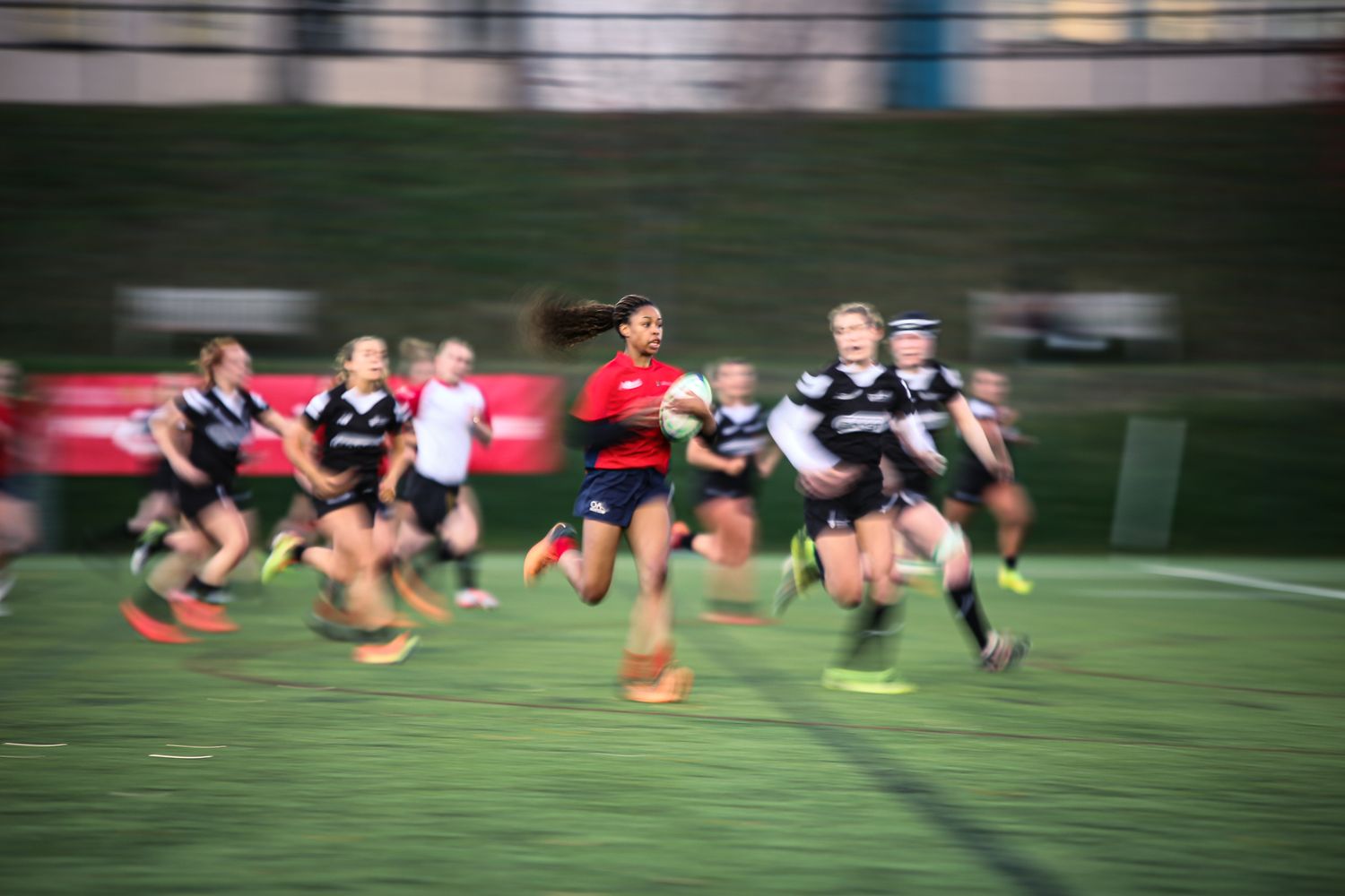 Motion-blurred rugby players running with the ball during a match on an outdoor field.