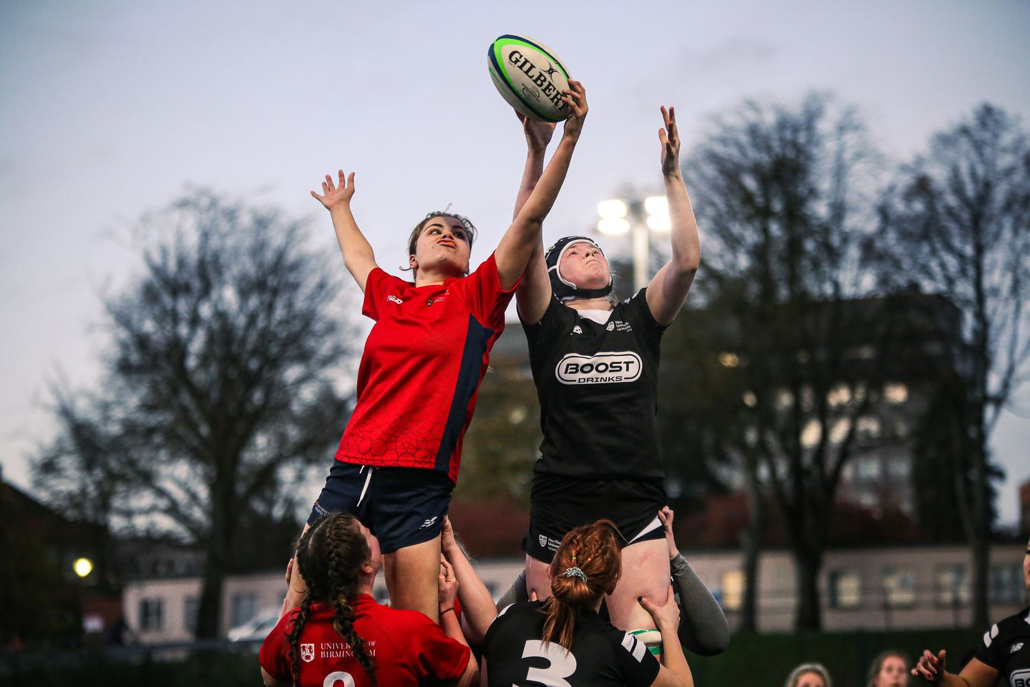 Athletes jumping and reaching for a ball during an outdoor sports competition.