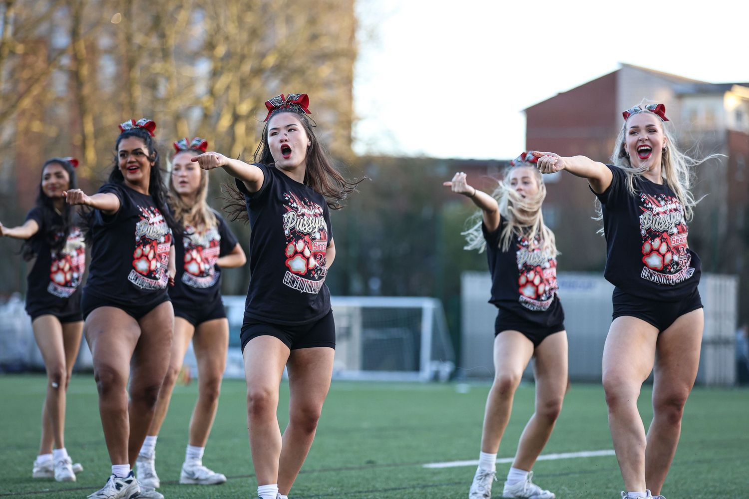 Dance squad members perform synchronized leg movements in matching uniforms on grass field.