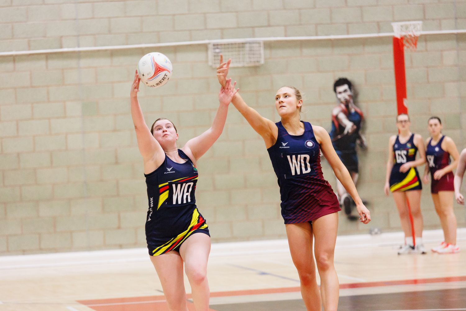 Indoor volleyball players leaping to spike the ball during a competitive match.