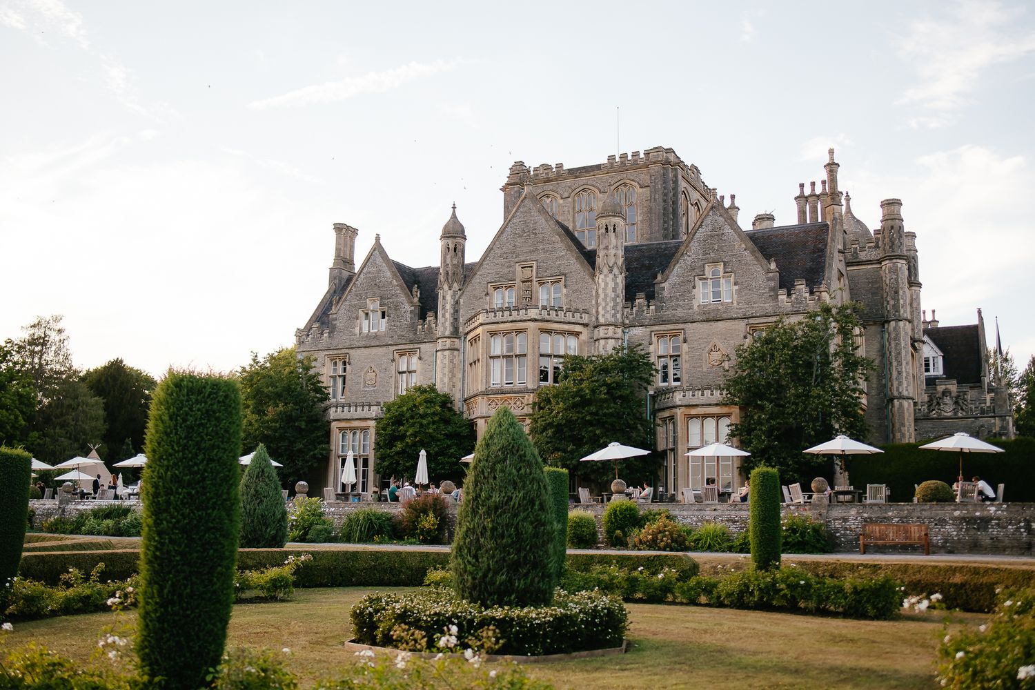 Panoramic view of a majestic stone mansion estate with manicured gardens and Gothic architecture.