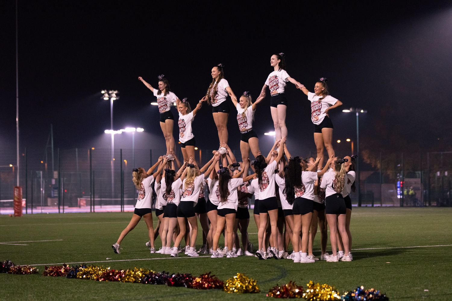Cheerleaders perform an impressive pyramid formation at night on an illuminated sports field.