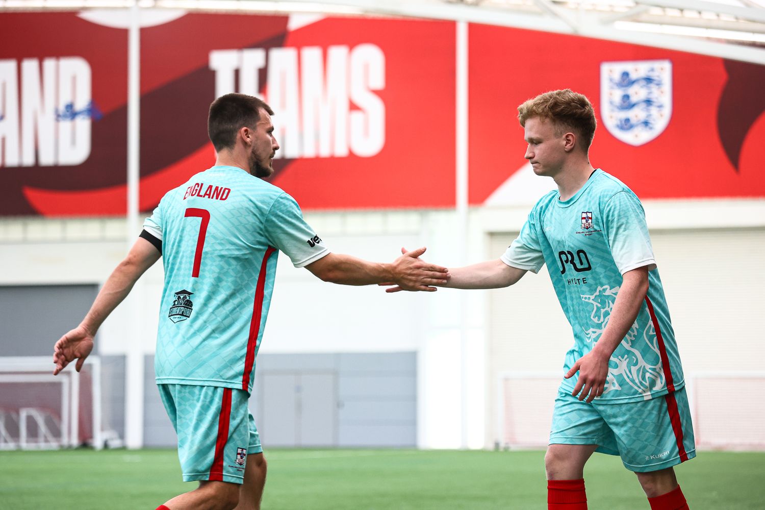 Soccer players in turquoise jerseys practicing on a training field with red signage in the background.