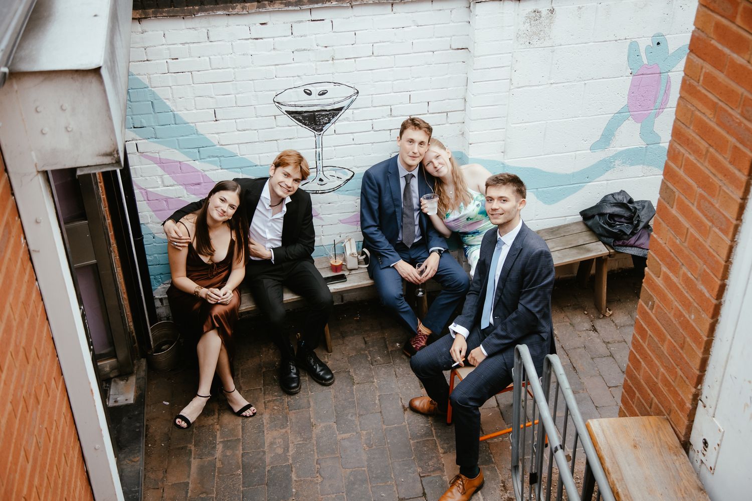 Wedding guests relaxing on outdoor patio with painted brick wall backdrop.