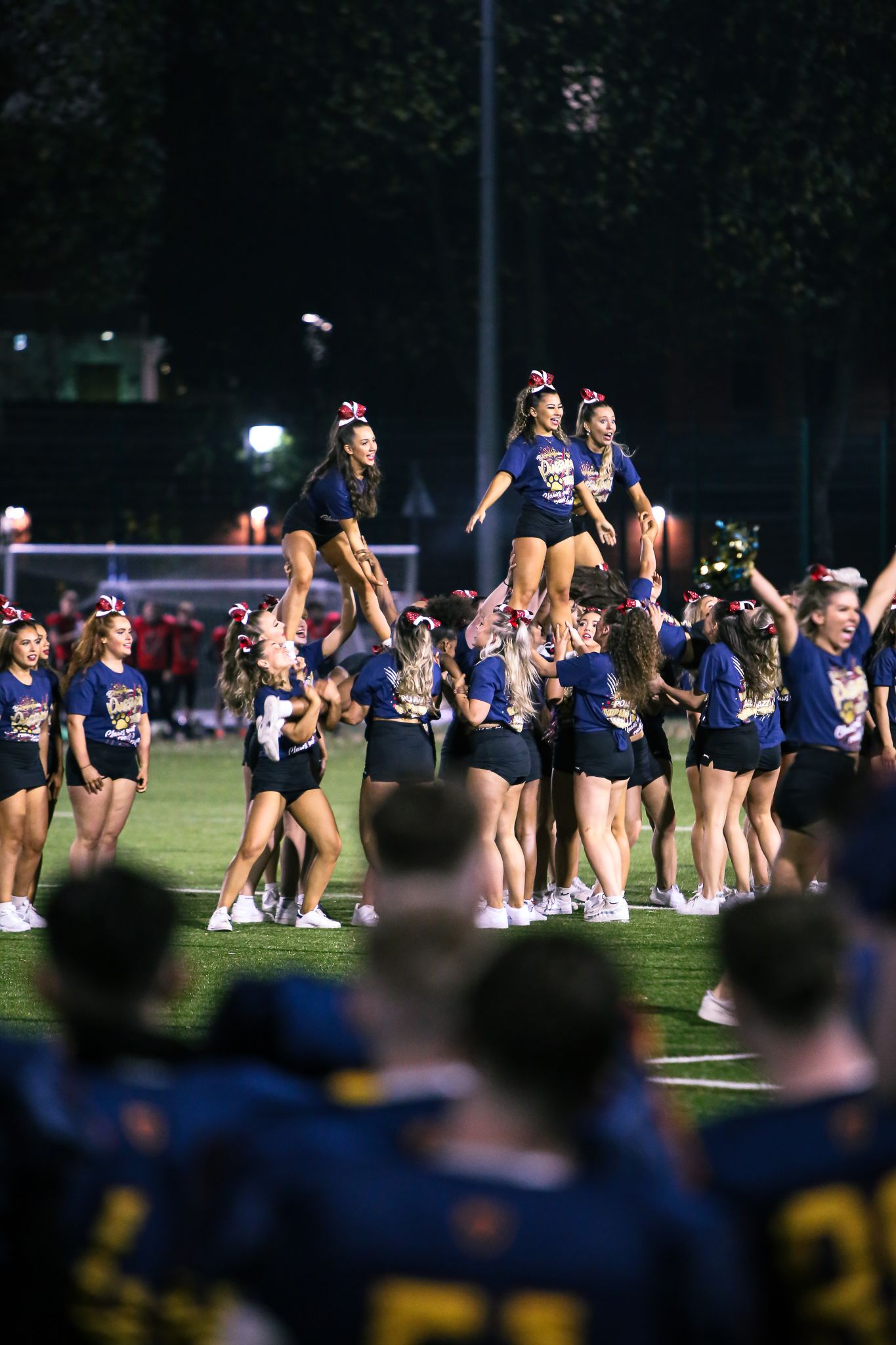 Cheerleaders perform during a nighttime sports event on a field under stadium lights.