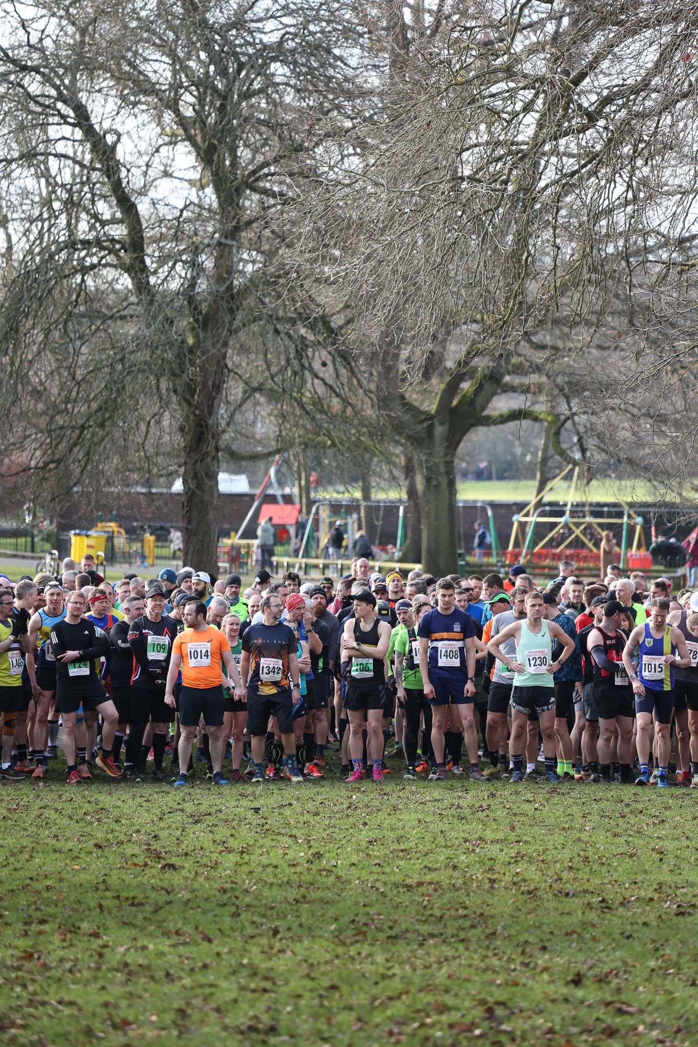 Large group of runners lined up at starting line under bare winter trees.