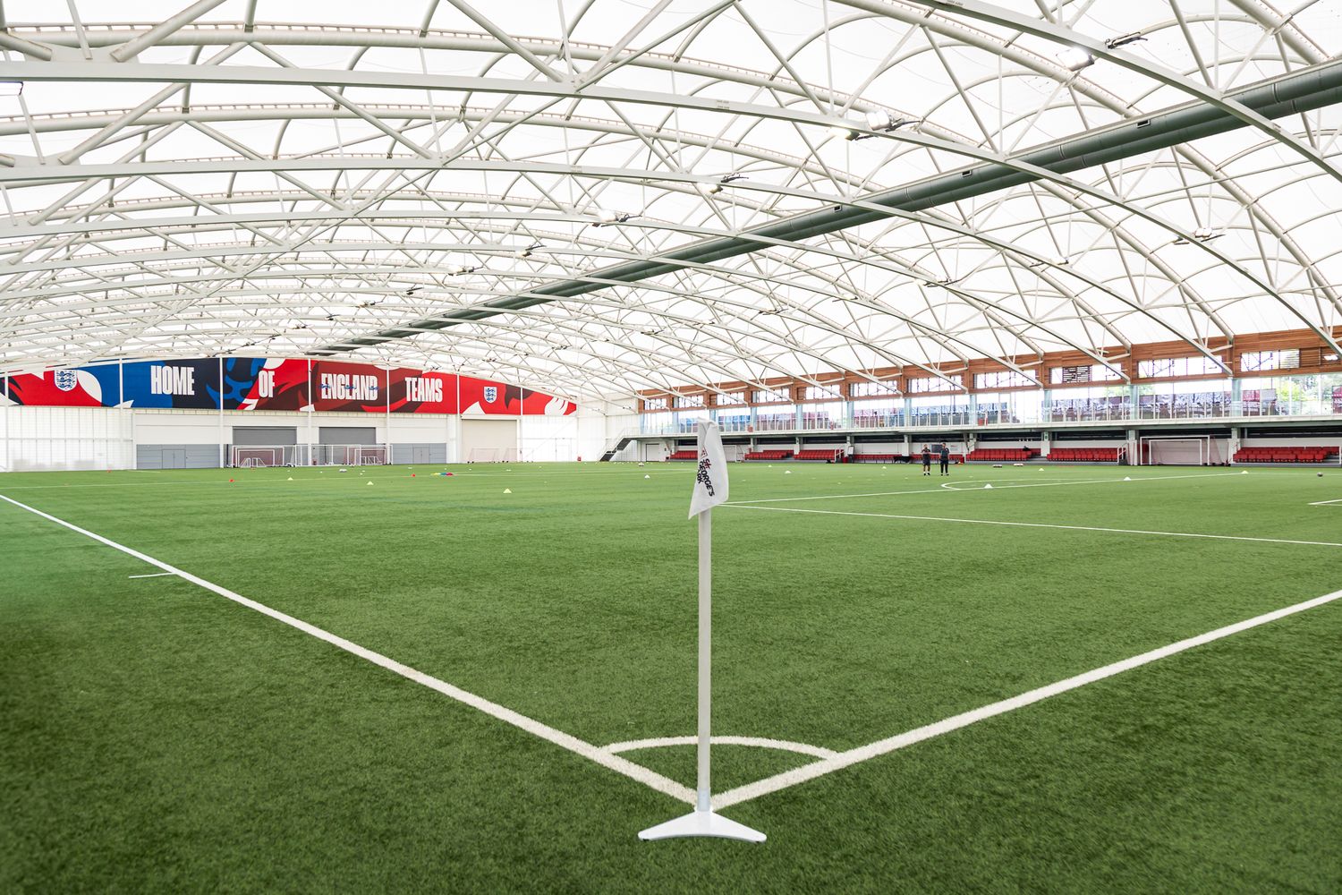 Wide angle view of indoor sports facility with white curved roof and artificial turf field.