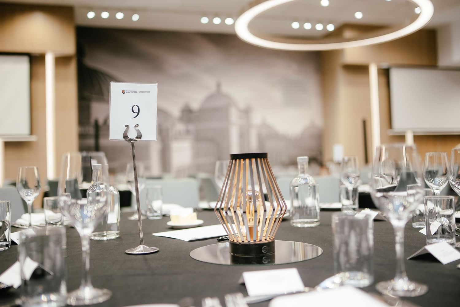 Elegant table setting at a formal event with a modern lantern centerpiece and crystal glassware in a banquet room.