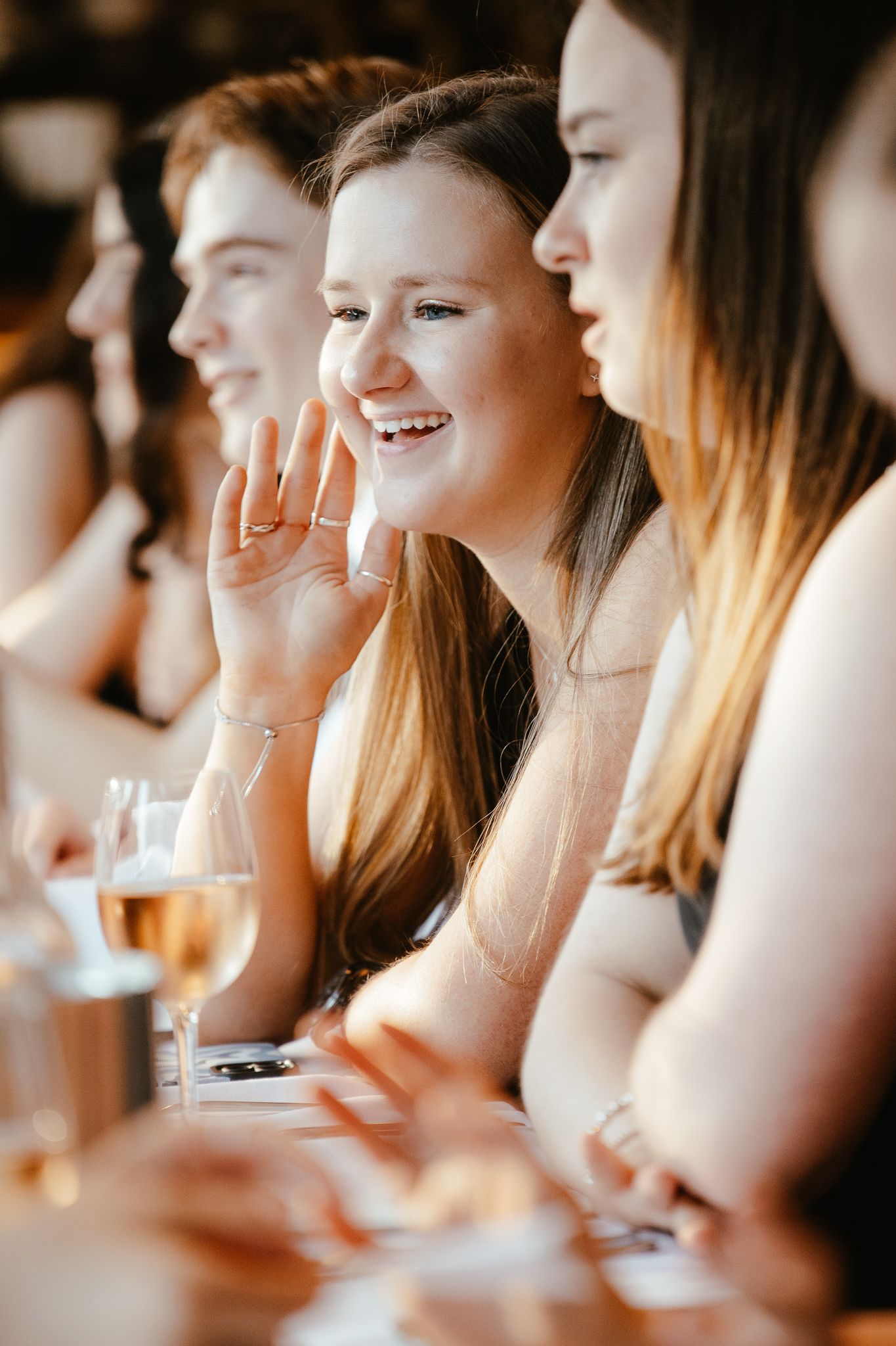 Row of guests smile and laugh while seated at a formal event.
