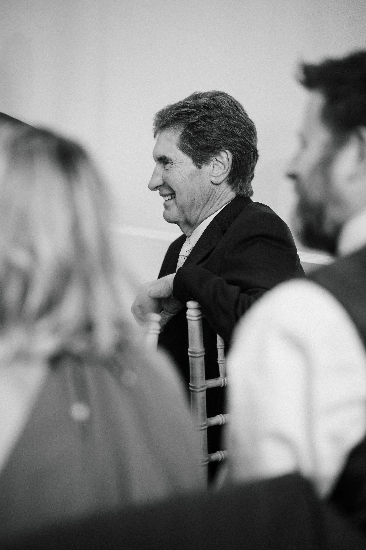 Black and white photo of a smiling middle-aged man in a suit seated at a formal event.