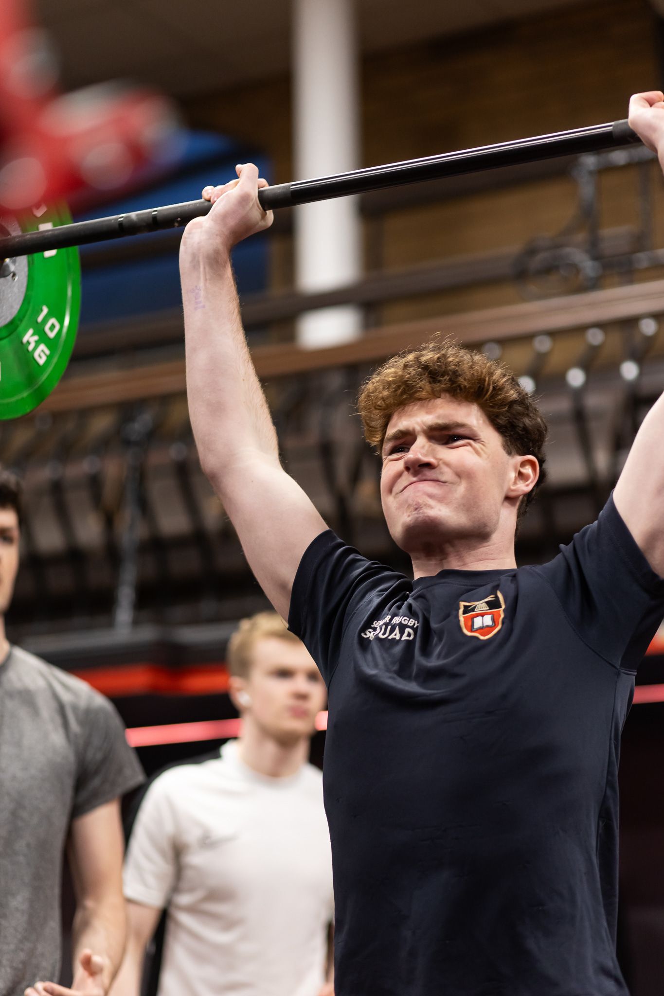 Athlete performing an overhead barbell lift with green weight plates in a gym.